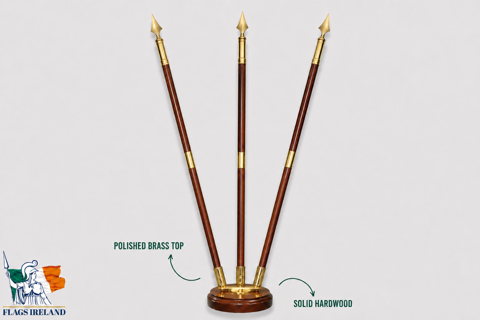 A set of three polished brass spear-like flagpoles with reddish-brown wooden shafts and a round wooden base, shown on a light gray background with text callouts reading 'POLISHED BRASS TOP' and 'SOLID HARDWOOD'. A Flags Ireland logo appears in the lower left corner.