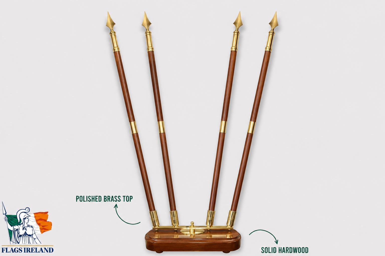 Four polished brass spear shafts with pointed tips mounted on a polished hardwood base, shown against a light gray background with text callouts highlighting the polished brass top and solid hardwood construction. A Flags Ireland logo appears in the lower left corner.