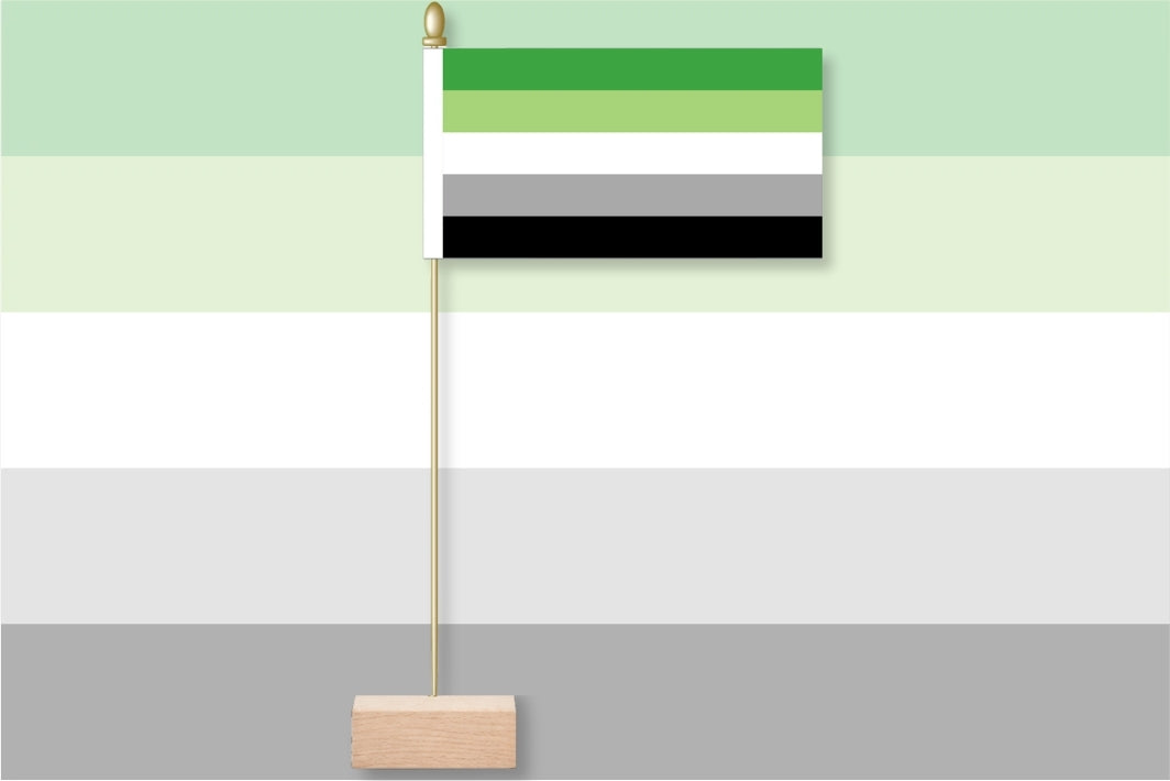 Flag with green, gray, and black stripes on a stand against a gradient background. Aromantic Pride Flag.