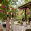 Group of women gathered around a table with decorations under a wooden shelter with colorful triangle bunting flags. Baby shower decoration.