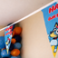 Birthday banner with cartoon character and 'Happy Birthday' text, hanging above colorful balloons.