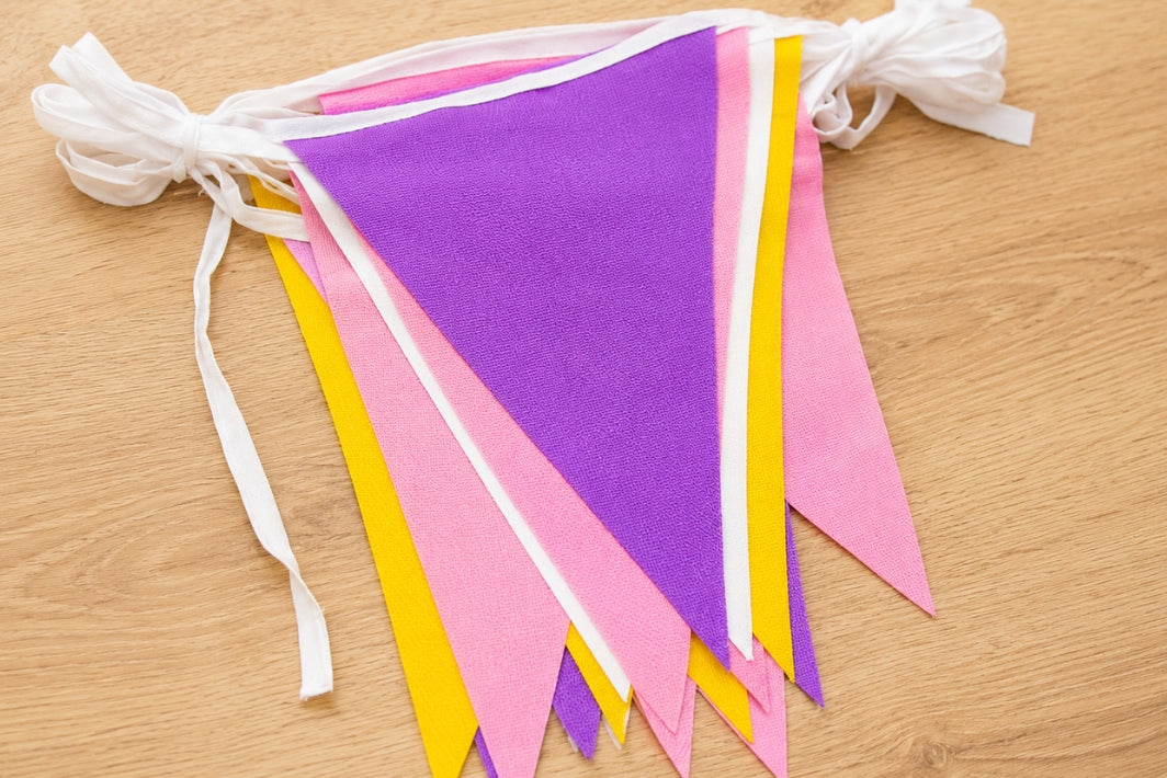 Purple, Golden Yellow and Pink triangle polyester bunting on a wooden surface