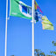 Two flags on poles against a clear blue sky with trees at the bottom.