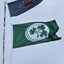 Two flags, one green with a shamrock design and the other blue with a red emblem, waving against a clear sky.