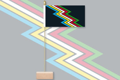 Colorful zigzag patterned flag with a wooden base on a gray background. Original Disability Pride