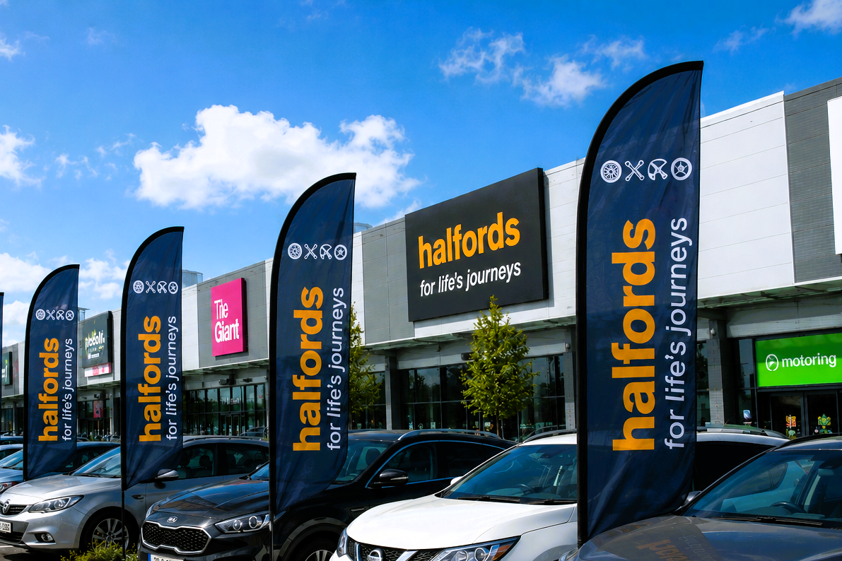 Halfords store with branded flags and cars in front on a clear day.