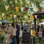 Community fair with colorful bunting, people, and a chalkboard sign in an outdoor setting.
