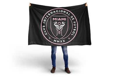 Person holding a black Inter Miami flag with Club Internacional de Fõtbol Miami logo