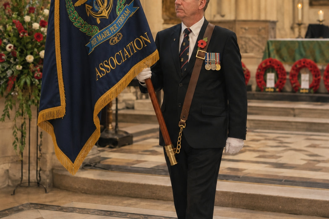 A man in a dark suit and tie stands indoors holding a blue ceremonial flag with gold fringe and the words 'Marine Corps Association.' The flag also shows an anchor emblem and gold lettering.