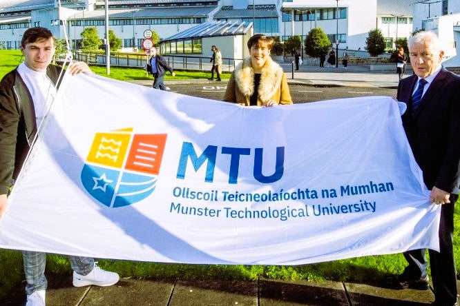 Three people holding a large banner with Munster Technological University logo and name.