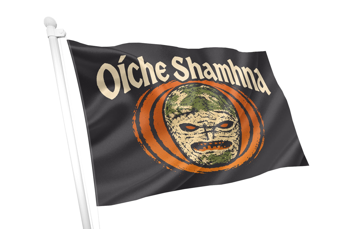 A black flag on a white pole featuring the text 'Oíche Shamna' in beige above a stylized mask inside an orange circular design, shown against a plain white background.