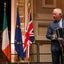 Prince Charles speaking at a podium with Irish, EU, and UK flags in the background.
