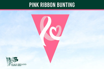 A pink triangular bunting flag with a white ribbon and heart design, shown against a light blue sky background. A dark green banner at the top reads 'PINK RIBBON BUNTING' and a 'Flags Ireland' logo is visible in the bottom left corner. Breast Cancer Bunting.