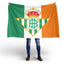 Person holding a Flag with a Real Betis logo featuring a crown and a letter 'B' on a green, white, and orange irish Flag background.