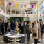 Open day event with people, tables, and colorful bunting flags in a large building.