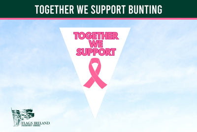 A digital graphic featuring a white triangular pennant design with pink text reading 'TOGETHER WE SUPPORT' and a pink awareness ribbon, set against a light blue sky background. A dark green banner at the top reads 'TOGETHER WE SUPPORT BUNTING', and the 'Flags Ireland' logo is in the bottom-left corner. Breast Cancer