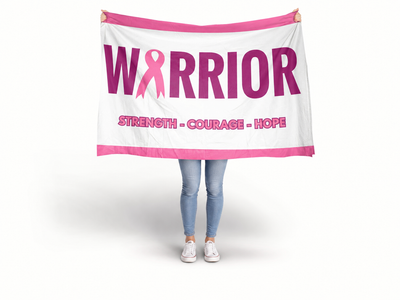 A person holding up a white fabric banner with pink trim and the word 'WARRIOR' in large pink letters, where the O is replaced by a pink ribbon. Smaller pink text below reads 'STRENGTH - COURAGE - HOPE. Breast Cancer Flag Banner.