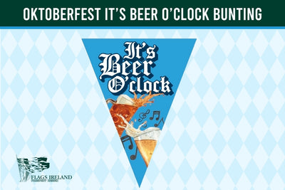 A triangular pennant banner design with the text 'It's Beer O'clock' in white gothic lettering, featuring an illustration of an orange beer glass with foam and musical notes, set against a blue background. The banner is displayed on a light blue and white harlequin patterned background with a dark green header banner reading 'OKTOBERFEST IT'S BEER O'CLOCK BUNTING' and a 'Flags Ireland' logo in the bottom left.